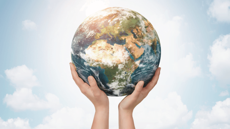 Two hands holding model of planet Earth up against a blue, cloudy sky